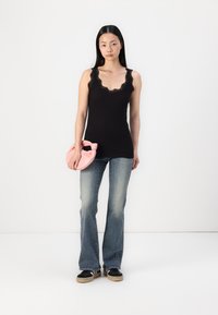 Top sin mangas negro con encaje, combinado con jeans acampanados de color azul claro y zapatillas negras. Sosteniendo un bolso de tela rosa.
