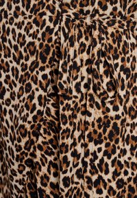Detailní záběr na látku s leopardím potiskem s uvázaným pásem v pase a řaseným švem na hnědém, černém a béžovém textilu.
