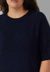 Marineblauer Strickpullover mit runder Ausschnitt und halblangen Ärmeln, der eine weiche Textur und gerippte Bündchen aufweist. Keine sichtbaren Muster oder Akzente.