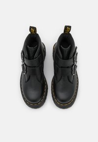 Black leather ankle boots with two straps and metal buckles. Features yellow stitching along the sole and a black textured finish.