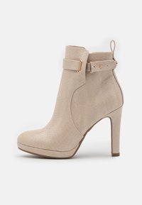 Bottine beige à talon haut avec motif serpent texturé, bride latérale avec boucle dorée et bout arrondi sur fond blanc.