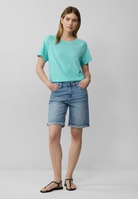 Turquoise t-shirt met korte mouwen en een ronde hals, gecombineerd met lichtblauwe denim shorts met opgerolde manchetten en zwarte sandalen met bandjes.