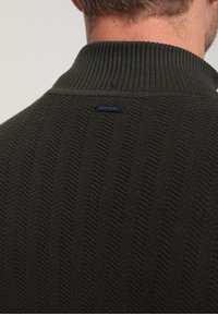 Dunkelgrüner Pullover mit ribbeltem Kragen, der ein strukturiertes Strickmuster aufweist und ein kleines blaues Logoschild am Nacken hat.