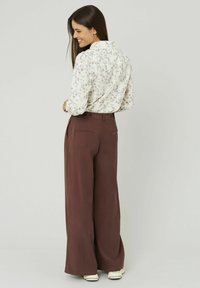 Blouse blanche à motifs floraux avec un col à volants, associée à un pantalon large bordeaux taille haute doté de poches arrière et de boutons décoratifs.