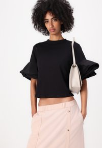 Schwarzes verkürztes T-Shirt mit Puffärmeln, kombiniert mit einem hellrosa Rock mit elastischem Bund, der dekorative Knöpfe und seitliche Taschen hat.