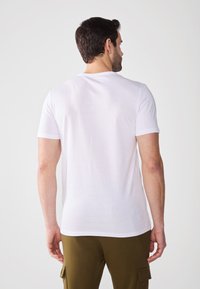 Bílá krátká trička s krátkým rukávem vyrobená z měkkého materiálu, s klasickým kulatým výstřihem a jednoduchým designem, spárovaná se zelenými cargo kalhotami.