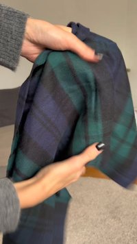 Flanelska tkanina v temno zeleni in mornarski modri karirasti vzorec, z mehko teksturo. Roka drži tkanino, kar prikazuje njeno padajočnost in fleksibilnost.