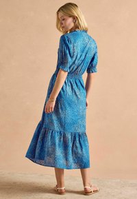 Modrá midi šaty so vzorom, krátkymi puffovými rukávmi, elastickým pásom a vrstvovou volánovou sukňou. Hladká tkanina, pohodlný strih a dĺžka po členky.