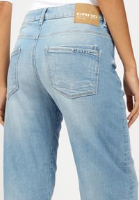Light blue denim jeans with a relaxed fit, featuring back pockets, a visible logo patch, and a textured fabric.