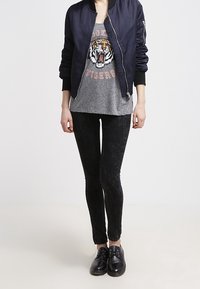 Marinblå bomberjacka över en grå T-shirt med en tiger grafik, matchad med svarta skinny jeans och svarta snörskor.