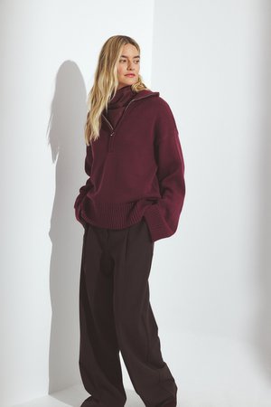 Suéter de punto burdeos con cuello con media cremallera, dobladillo acanalado y hombros caídos, combinado con pantalones sueltos de color marrón oscuro.