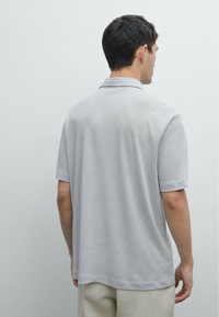 Světlě šedé polo tričko vyrobené z jemné látky, s krátkými rukávy a klasickým límcem. Jednoduchý design bez viditelných vzorů nebo akcentů.
