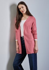 Cardigan aperto davanti, con maniche lunghe, in maglia rosa soft, indossato sopra una maglietta bianca e abbinato a jeans a gamba larga blu scuro. Texture liscia.