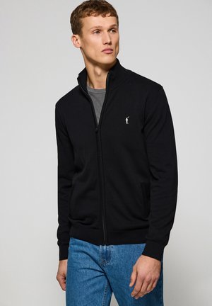 Schwarze Zip-Up-Sweatjacke mit hohem Kragen, ausgestattet mit einem kleinen weißen Logo. Der Stoff ist glatt und sie hat seitliche Taschen sowie gerippte Bündchen.