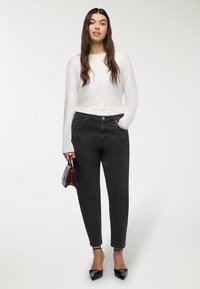 Czarne spodnie dżinsowe z wysokim stanem, o prostym kroju i pięcioma kieszeniami, zestawione z białą bluzką z długim rękawem i czarnymi, szpiczastymi wysokimi obcasami.