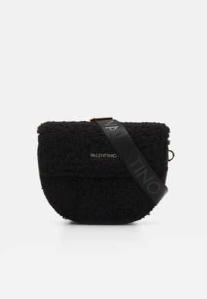 Sort fleece crossover taske med en rund form, guld logo detalje og en bred sort rem med brandnavnet i hævet skrift.