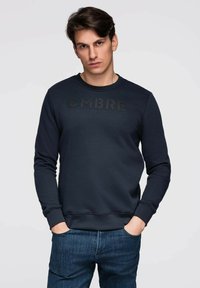 Felpa blu navy realizzata in tessuto morbido, con collo tondo e maniche lunghe. Sul petto è ben visibile un logo "OMBRE" nero opaco.