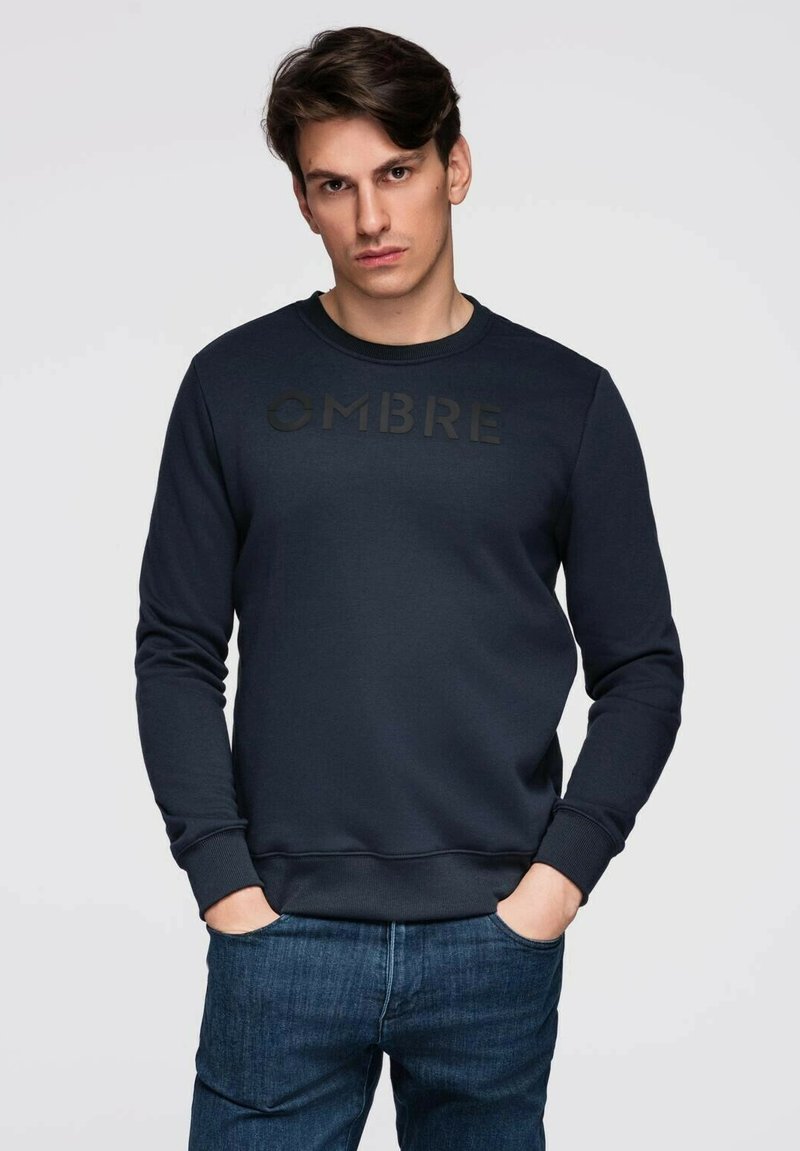 Felpa blu navy realizzata in tessuto morbido, con collo tondo e maniche lunghe. Sul petto è ben visibile un logo "OMBRE" nero opaco.