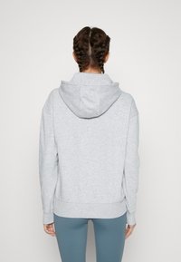 Sweat à capuche gris à coupe décontractée, avec poignets et ourlet côtelés. Tissu en mélange de coton au toucher doux. Vue de dos montrant une coiffure avec des tresses.