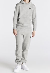 Grau Sweatshirt und Sweatpants-Set aus weichem Material, mit Kapuze und Logo auf der Brust, kombiniert mit weißen Sneakers.
