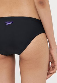 Svarta Speedo-simbyxor med lila logotyp, med en snygg design och mjukt tyg. Minimalistisk skärning med böljande kanter och subtil textur.