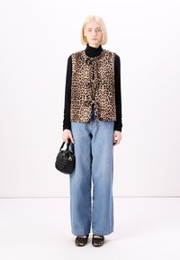 Γιλέκο με λεοπάρ σχέδιο, μαύρη μπλούζα με μακριά μανίκια, χαλαρές μπλε τζιν παντελόνες, μαύρη τσάντα και μαύρα παπούτσια. Το γιλέκο έχει υφασμάτινο σχέδιο και κορδόνια.