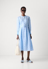 Light blue polka dot dress with long sleeves, button-down front, cinched waist, and a matching belt. Paired with light blue mules and a beige bag.