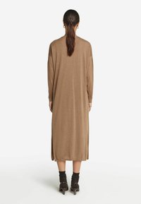 Brun stickad långärmad klänning med rak skärning, sidofickor och avslappnad passform, kombinerad med svarta ankelsockor och klackskor.