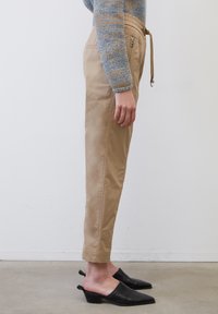 Beige taps toelopende broek met een elastische tailleband en trekkoord, met zij ritszakken. Gecombineerd met zwarte hakken mules.