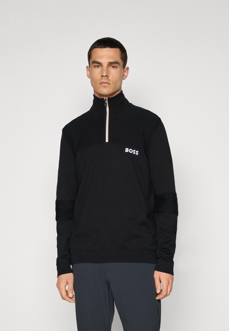 Svart zip-up genser med strukturert overdel, logo på brystet, og ribbede mansjetter. Har høy krage og kontrasterende glidelås.