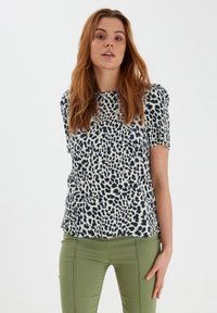 Top a maniche corte in tessuto stampato con una stampa leopardata blu navy su uno sfondo chiaro, abbinato a pantaloni verdi aderenti.