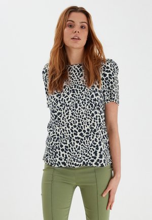 Top a maniche corte in tessuto stampato con una stampa leopardata blu navy su uno sfondo chiaro, abbinato a pantaloni verdi aderenti.