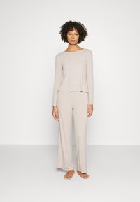 Helles beige Loungewear-Set bestehend aus einem Langarmoberteil mit lockerer Passform und passenden weit geschnittenen Hosen, gefertigt aus einem weichen, dehnbaren Stoff.