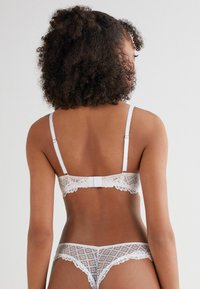 White lace lingerie set features intricate patterns, a delicate trim, adjustable straps, and a hook-and-eye closure at the back.