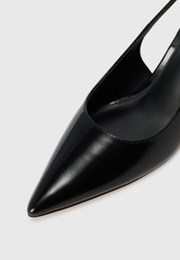 Juodas odinis slingback batų modelis su smailiu pirštu, lygia tekstūra ir minimalistiniu dizainu, turintis išpjovą šone ir liesą kulną.
