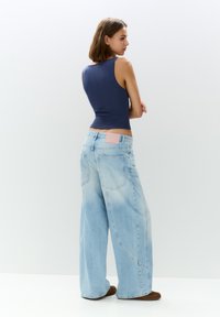 Top senza maniche di colore blu navy abbinato a jeans larghi di colore azzurro chiaro con un'etichetta rosa sul retro in vita. Tessuto morbido con una vestibilità comoda.