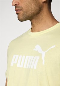 Light yellow cotton t-shirt featuring a white "PUMA" logo and a leaping puma graphic. Short sleeves and round neckline. Soft texture.