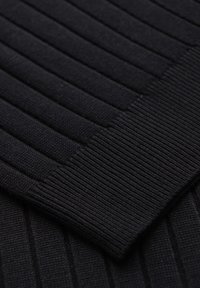 Gros plan d'un tissu tricoté côtelé noir montrant la texture détaillée et les différentes largeurs de côtes dans le matériau.