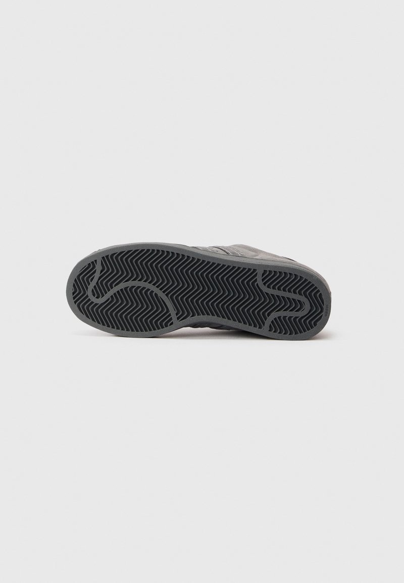 Semelle de chaussure avec une surface en caoutchouc noir à motif, présentant un profil en zigzag pour l'adhérence et la durabilité, montrant une légère usure près des bords.