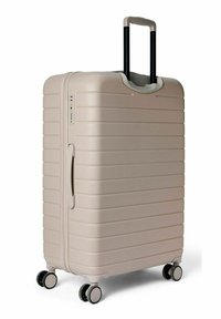 Valise rigide beige clair avec surface texturée, rainures verticales, poignée noire rétractable et quatre roues pivotantes pour une mobilité optimale.
