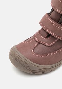 Brązowy boot na rzep z różowym przeszyciem, teksturowana syntetyczna cholewka i wytrzymała gumowa podeszwa, z okrągłym czubkiem i wzmocnioną konstrukcją.