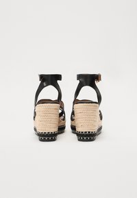 Sandales compensées en cuir noir avec des détails en jute tressé, une sangle de cheville réglable et une semelle texturée. Des accents de couture noire soulignent le design.