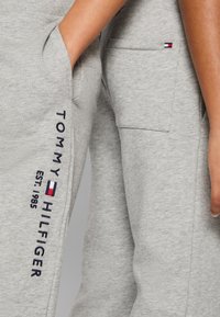Harmaat puuvillaiset verkkarit, joissa on sivutaskut, varustettu brodeeratulla "TOMMY HILFIGER" -logolla ja lipputyylillä punaisessa, valkoisessa ja sinisessä.