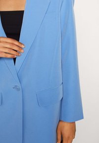 Lichtblauwe blazer met een klassiek ontwerp, reverskraag, twee voortassen en een enkele knoopsluiting, gemaakt van zachte stof.