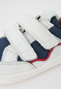 Hvite og marineblå sneakers laget av mesh og lær. Har borrelåsremmer, røde detaljer og en teksturert såle.