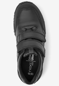 Chaussure pour enfant noire avec tige synthétique, deux bandes Velcro, col rembourré et accents texturés. L'étiquette de taille indique "next 12 (G)".