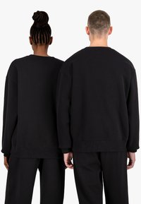 Sudaderas negras de gran tamaño con mangas largas, puños y dobladillo acanalados. Tejido de mezcla de algodón suave. Vista desde la parte trasera, con un minimalismo en la marca.