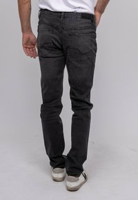 Jean en denim noir à coupe slim, avec des poches arrière et un léger délavage. Associé à des baskets blanches.