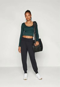Fekete jogger nadrág, sötétzöld, hosszú ujjú crop top, fehér sneakers és fekete táska. Sima anyag, laza fazon, egyszerű dizájn és minták nélkül.