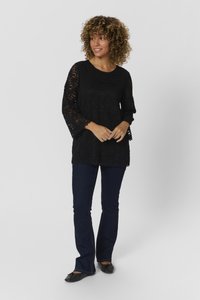Black lace top with three-quarter sleeves, scalloped hem, worn over dark blue flared jeans and black flat shoes. Background is plain white.